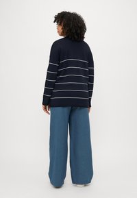 Marineblauwe trui met witte horizontale strepen, gecombineerd met brede blauwe broek. Zachte stof, ontspannen pasvorm, naadloos ontwerp en lange mouwen.