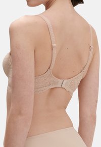 Beige pitsikleidiga rinnahoidja reguleeritavate rihmadega, lillemustriga ja taga konksu ja silmadega sulgemisega, näidates siledaid ja tekstureeritud kangaid.