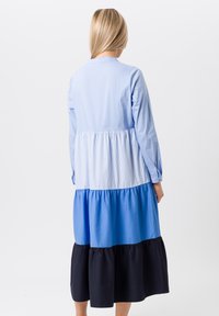 Blauwe meerlagige jurk met lange mouwen, met een gestreepte lijfje en effen blauwe en marineblauwe lagen. Gemaakt van zachte stof, met een vloeiende uitstraling.