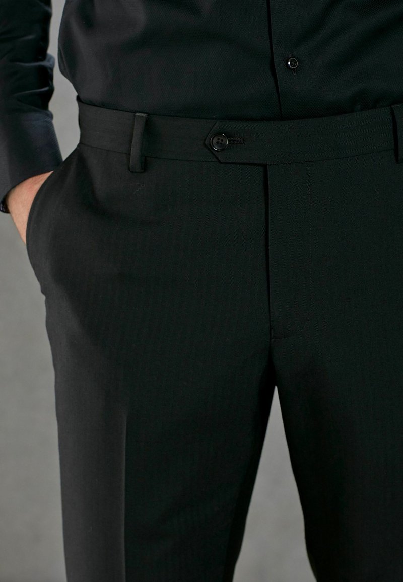 Pantalons noirs en tissu plat, avec de subtils rayures verticales, une fermeture à un bouton et des poches latérales. Coupe ajustée et texture lisse.