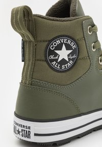 Bottes Converse Chuck Taylor All Star vert olive avec textile résistant à l'eau, col rembourré, patch logo noir et semelle en caoutchouc blanc avec des rayures noires.