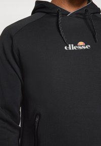 Black zip-up hoodie featuring a grey logo on the chest, textured fabric, adjustable drawstring hood, and a zippered side pocket.