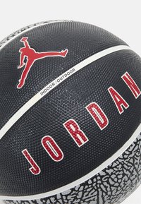 Svart basketball med teksturert overflate, rød "JORDAN" tekst og ikonisk Jumpman-logo; har en hvit stripe merket "INDOOR/OUTDOOR."