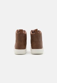 Brune skinn høyde sneakers med teksturert overflate, polstret krage og hvit gummisåle; har en tabbak for enkel påføring.