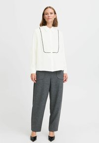 White long-sleeve shirt with black piping, collared neckline. Gray plaid, relaxed-fit trousers with front pockets. Black pointed flats.