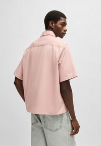 Korte mouwen roze button-up shirt met een relaxte pasvorm, gladde textuur en achterstukdetail, gecombineerd met lichtgrijze baggy jeans.