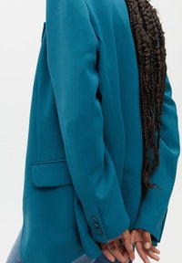Blazer turquoise à coupe décontractée, fermeture à un bouton, poches latérales et poignets à boutons. Tissu lisse avec une légère brillance.