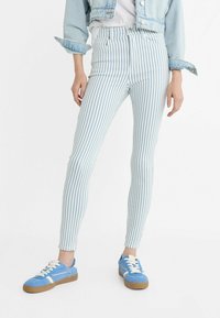 Niebieskie i białe w paski rurki z wysokim stanem, połączone z niebieskimi trampkami. Na koniec look dopełnia dżinsowa kurtka z podwiniętymi rękawami.