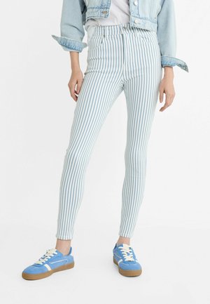 Blå og hvide stribede skinny jeans med høj talje, parret med blå sneakers. En denimjakke med opsmøgede ærmer fuldender looket.