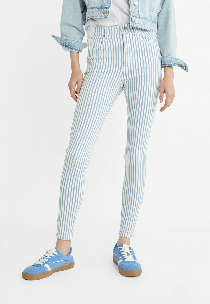 Niebieskie i białe w paski rurki z wysokim stanem, połączone z niebieskimi trampkami. Na koniec look dopełnia dżinsowa kurtka z podwiniętymi rękawami.