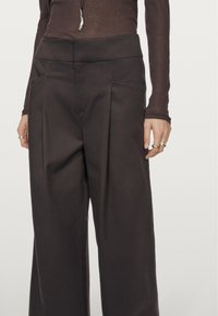 Bruine wijde broek met hoge taille, voorzien van zijzakken en accentstiksel. Glad textuur en minimalistisch ontwerp.