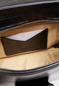 Black leather interior of a bag showing a card holder pocket and a folded card with "Merci" text on cream paper. Smooth fabric lining.