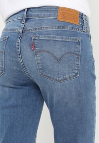 Vaqueros de mezclilla azul con corte recto. Las características incluyen un parche de cuero en la parte posterior, bolsillos traseros distintivos con un patrón de costura y un lavado claro.