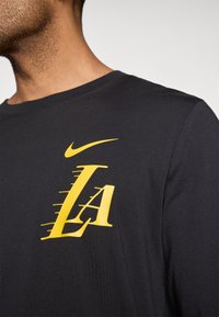 Fekete hosszú ujjú póló nagy sárga "LA" grafikával és Nike logóval a bal mellrészen. Puha anyag, környakú dizájnnal.