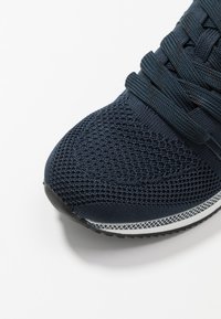 Marineblaue Sportschuhe mit einem strukturierten Mesh-Obermaterial, flachen Schnürsenkeln und einer schwarzen Gummisohle mit einem weißen Akzentstreifen.