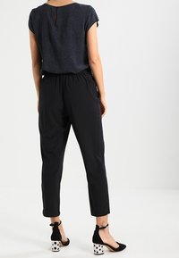 Černé zúžené kalhoty s elastickým pasem párované s vzorovaným námořnickým topem, který má krátké rukávy a detail klíčové dírky na zádech. Černé lodičky s bílými puntíky.