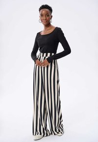 Czarna bluzka z długim rękawem w połączeniu z wysokim stanem, szerokimi spodniami w odważne czarno-kremowe pionowe paski. Tkanina o teksturze, luźny krój.