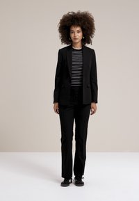 Černý oblek s jedním knoflíkem, doplněný černobílou pruhovanou košilí a slim fit kalhotami. Vyznačuje se elegantním designem a minimem doplňků.