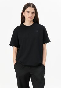 T-shirt en coton noir avec un col rond, des manches courtes et un logo discret sur la poitrine. Associé à un pantalon noir.