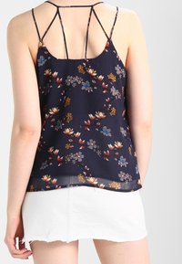 Woman wearing a navy floral sleeveless top with thin straps and a white denim mini skirt, shown from the back against a plain background.