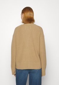 Brązowy sweter z dzianiny o prążkowanej fakturze, z rękawami raglanowymi i luźnym krojem. Dół swetra jest nieco dłuższy z tyłu. Idealnie pasuje do niebieskich dżinsów.