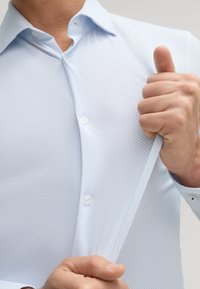 Lichtblauwe overhemd met een textuurpatroon, met een button-down kraag en witte knopen. De stof lijkt glad en ademend.