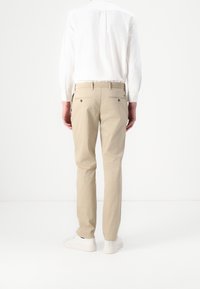 Beżowe spodnie wykonane z bawełny w prostym kroju. Posiadają dwa tylne kieszenie i są stylizowane z białymi trampkami oraz białą koszulą.