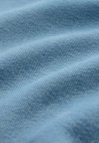 Gros plan de tissu en denim bleu clair montrant une fine texture de tissage diagonal et de légers plis.
