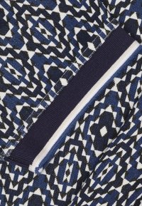 Geweven stof met geometrische ontwerpen in marineblauw, zwart en wit. Bevat een geribbelde marineblauwe accentrand met witte strepen aan de rand.