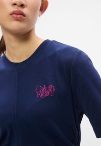 T-shirt a maniche corte blu navy in cotone con scollatura rotonda. Presenta il logo "Calvin Klein" ricamato in rosa sul lato sinistro del petto.