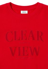 Sweatshirt en coton rouge avec un col rond, comportant des textes embossés "CLEAR VIEW" et "MINDS REFLECTION" en rouge plus foncé. L'étiquette de la marque indique "CECIL."