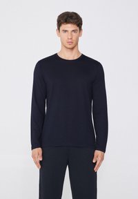Marineblaues Langarmshirt mit Rundhalsausschnitt, aus glatter Baumwolle, kombiniert mit dunklen Hosen. Minimalistisches Design ohne sichtbare Muster oder Hardware.