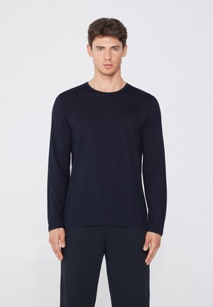 Marineblaues Langarmshirt mit Rundhalsausschnitt, aus glatter Baumwolle, kombiniert mit dunklen Hosen. Minimalistisches Design ohne sichtbare Muster oder Hardware.