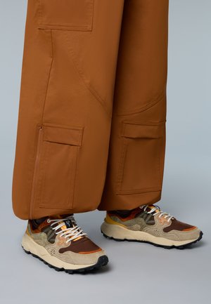 Cargo-Hosen in warmem Braun mit Reißverschlusstaschen; Sneakers in erdigen Farbtönen mit gemischten Materialien, strukturierten Akzenten und einer klobigen Sohle.