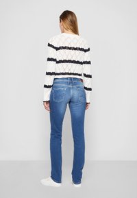 Vit och marinrandig stickad kort tröja, kombinerad med blå raka jeans. Lätt tyg med en öppen stickad textur och bakfickor.