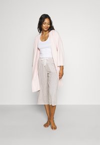 Light pink, textured robe with wide sleeves over a white tank top. Paired with striped, cropped pants featuring an elastic waistband.