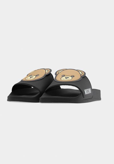 Sandales slides noires avec des visages d'ours en peluche souriants sur les brides et le logo "Moschino" sur les côtés, présentées sur un fond blanc.