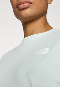 Φωτεινό μέντα πράσινο βαμβακερό μπλουζάκι με στρογγυλή λαιμόκοψη, με λευκό λογότυπο "The North Face" στην αριστερή πλευρά του στήθους.