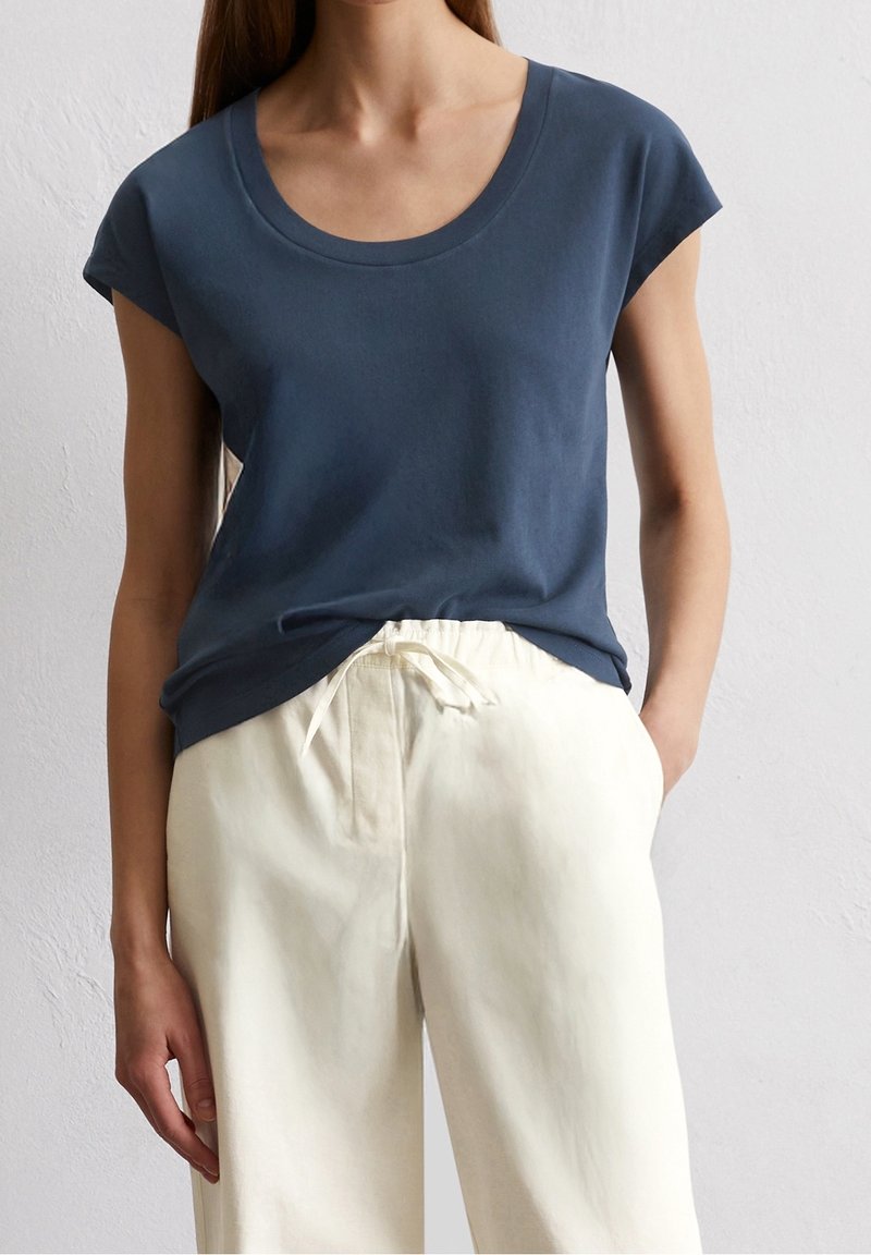 Tummansininen lyhythihainen paita pyöreällä kaula-aukkolla, yhdistettynä kermaisiin leveälahkeisiin housuihin, joissa on nauhakuuluvu. Sileä puuvillakangas.