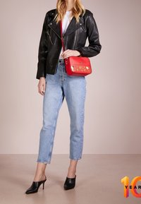 Giacca da moto in pelle nera, top bianco, jeans azzurri chiari, scarpe con tacco nere e una borsa a tracolla rossa con motivi a cuore dorati.