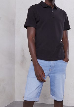 T-shirt polo noir avec col, portée avec un short en denim bleu clair. Le short est roulé au niveau de l'ourlet, mettant en valeur une coupe décontractée et confortable.