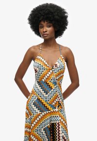 Vestido multicolorido con patrones en forma de zigzag en naranja, azul y blanco. Hecho de una tela ligera, tiene un escote en V profundo y tirantes de espagueti.
