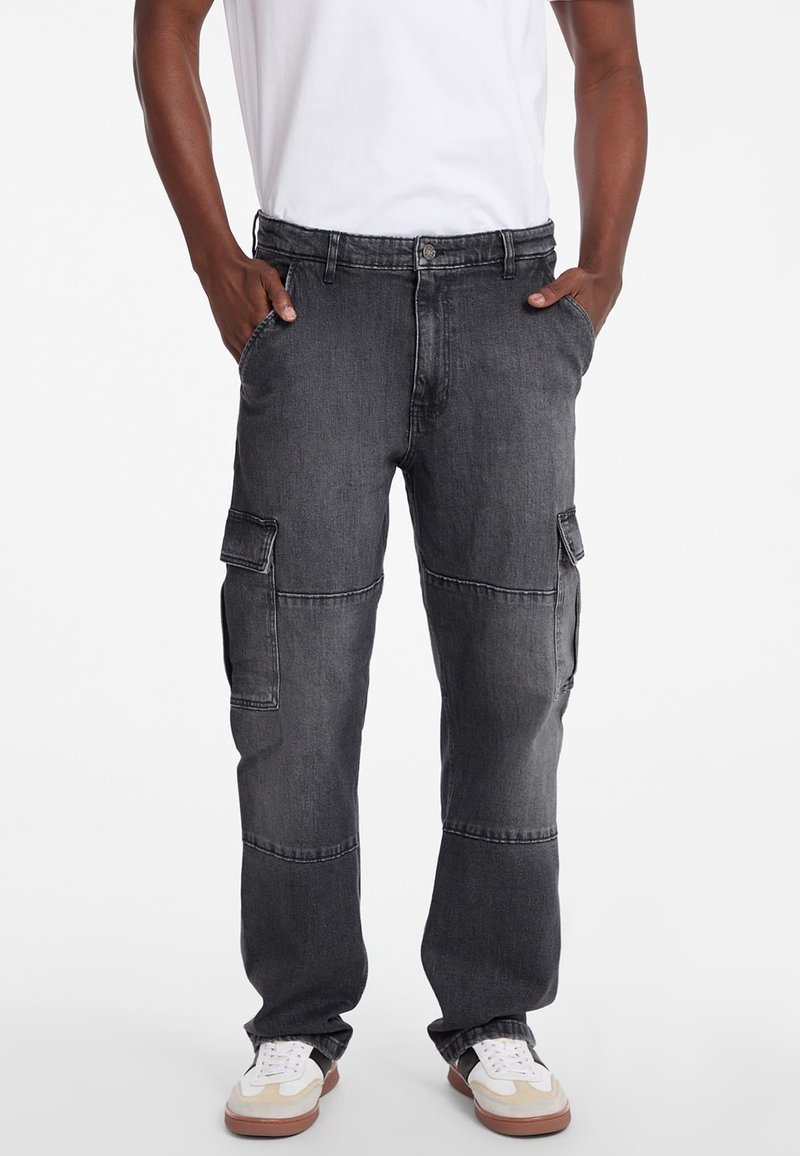 Pantaloni cargo gri închis din denim, cu buzunare laterale, croială lejeră și design cu picior drept. Asortați cu adidași albi.