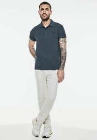 Mörkblå pikétröja med krage, korta uppvikta ärmar och en diskret logotyp. Kombinerad med ljusa, löst sittande byxor och sneakers.