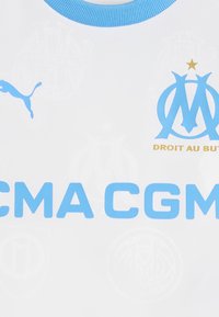 Bijela majica s svijetloplavim naglascima, Puma logotipom, EM emblemom i tekstom "CMA CGM". Tekstura izgleda glatko s suptilnim detaljima uzorka.