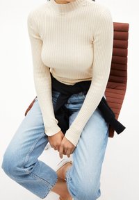 Beige geribbelde coltrui gecombineerd met lichtblauwe denim jeans. De trui heeft lange mouwen en een aansluitend model.