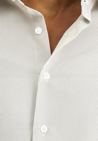 Camicia a righe grigio chiaro con colletto a punta e bottoni bianchi. Il tessuto ha una consistenza liscia con sottili righe verticali.