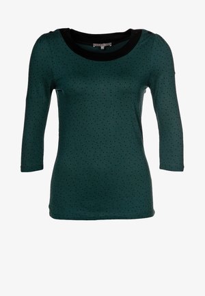 Dunkelgrünes, figurbetontes Langarmshirt mit kleinen schwarzen Punkten und einem schwarzen, rundem Halsausschnitt.