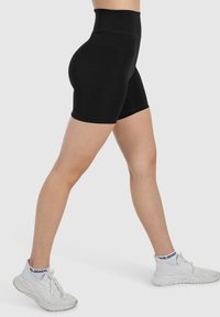 Pantaloni corti neri a vita alta realizzati in tessuto elasticizzato, con una superficie liscia e un design aderente che si estende fino a metà coscia.