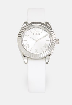 Sølvur med en hvid silikonesnor, rund urskive, tekstureret bezel og romerske tal som markører. Mærkenavnet "GUESS" vist på skiven.